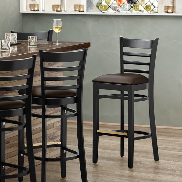 A Lancaster Table & Seating black wood ladder back bar stool with a dark brown vinyl seat.
