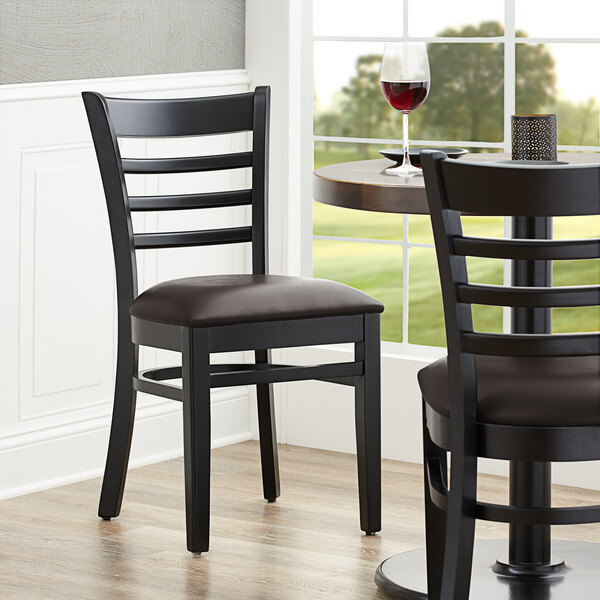 A pair of Lancaster Table & Seating black wood chairs with dark brown vinyl seats at a table in a restaurant.