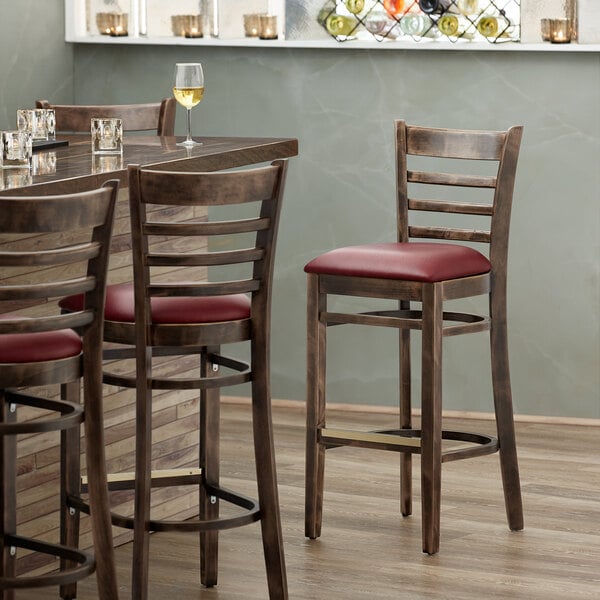 A Lancaster Table & Seating wood ladder back bar stool with a burgundy vinyl seat on a table in a restaurant dining area.