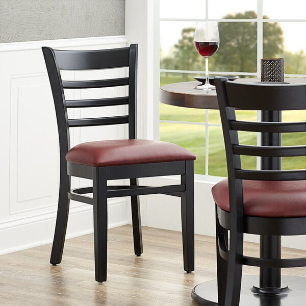 A Lancaster Table & Seating black wood chair with a burgundy vinyl seat at a table in a restaurant.