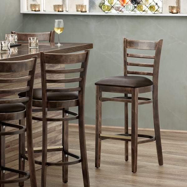 A Lancaster Table & Seating wood ladder back bar stool with dark brown vinyl seat at a table in a restaurant.