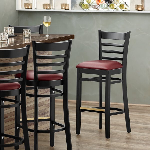 A Lancaster Table & Seating black wood ladder back bar stool with a burgundy vinyl seat.