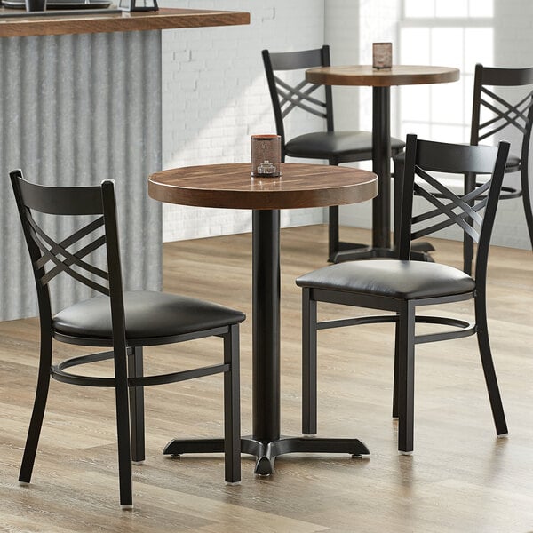A Lancaster Table & Seating round butcher block table with a cast iron base and black chairs in a restaurant.