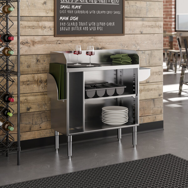 A stainless steel bussing and waitress station with shelves, a pan holder, and side compartments for napkins or trays.