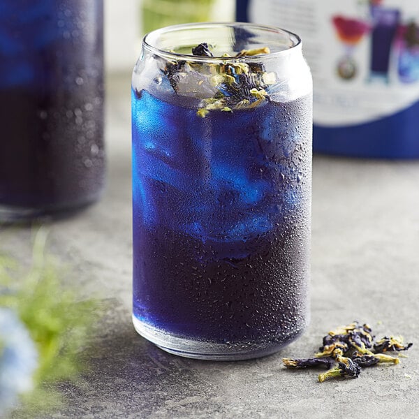 A glass of blue Wild Hibiscus Butterfly Pea Flower lemonade with flowers in it.