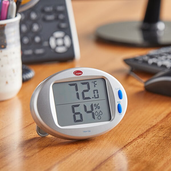 A Cooper-Atkins digital thermometer and hygrometer on a table in a professional kitchen.