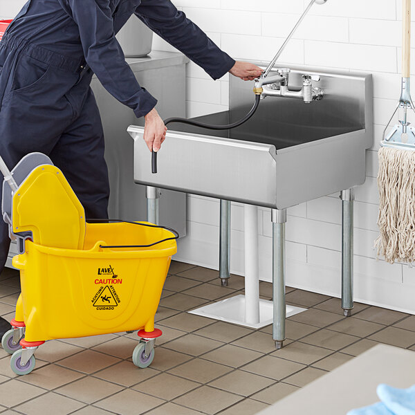 A person in a blue uniform using a hose to wash a Steelton standing mop sink.