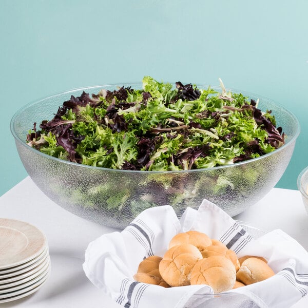 A pebbled salad bowl filled with lettuce on a table with a bowl of bread.