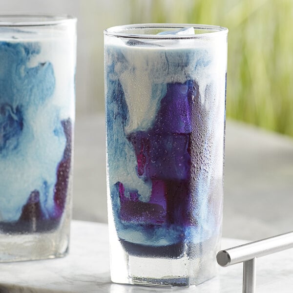 Two glasses of blue and purple Wild Hibiscus Butterfly Pea Flower Blue Matcha Tea on a white counter.