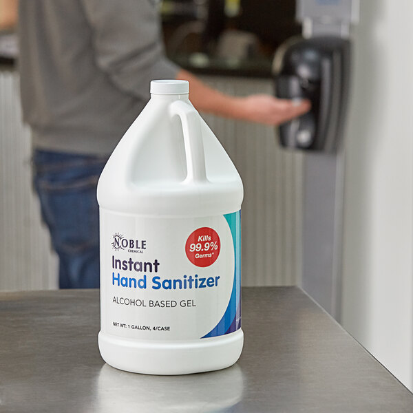 A man holding a white bottle of Noble Chemical alcohol-based hand sanitizer with a blue and white label and a pump.