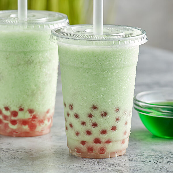 A green and white bubble tea with green leaves in the background.