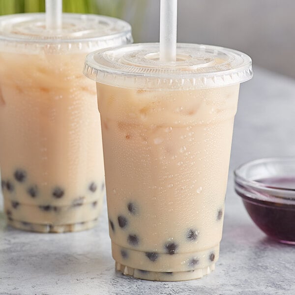Two plastic cups of lavender bubble tea with straws and a bowl of lavender liquid.