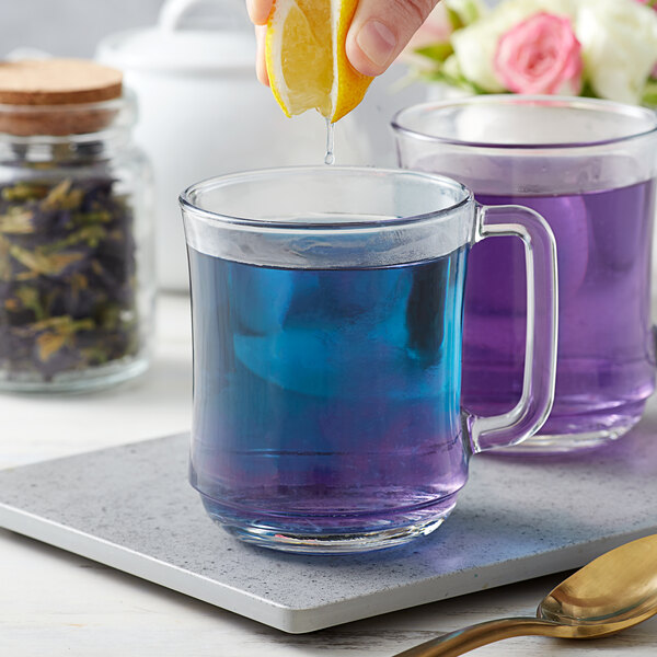 A hand squeezing a lemon over a glass of Bossen dried butterfly pea flower tea, turning the liquid blue.