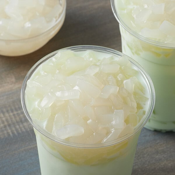A cup of milk with chunks of white coconut jelly on top.