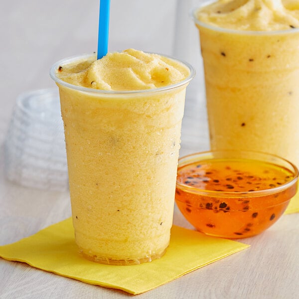 A yellow smoothie in plastic cups with straws and a bowl of yellow liquid.