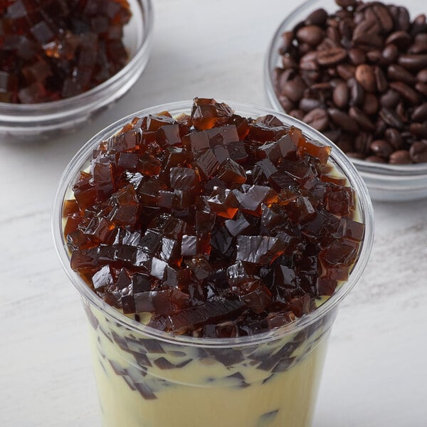 A cup of coffee with brown gelatin in it next to a container of Bossen Coffee Jelly.