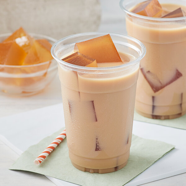 A group of plastic cups of brown liquid with orange jelly cubes.