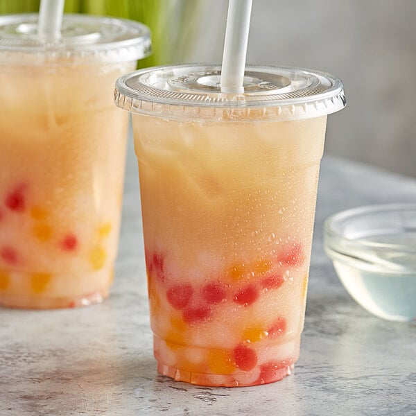 Two plastic cups with straws and yellow and red lychee drinks.
