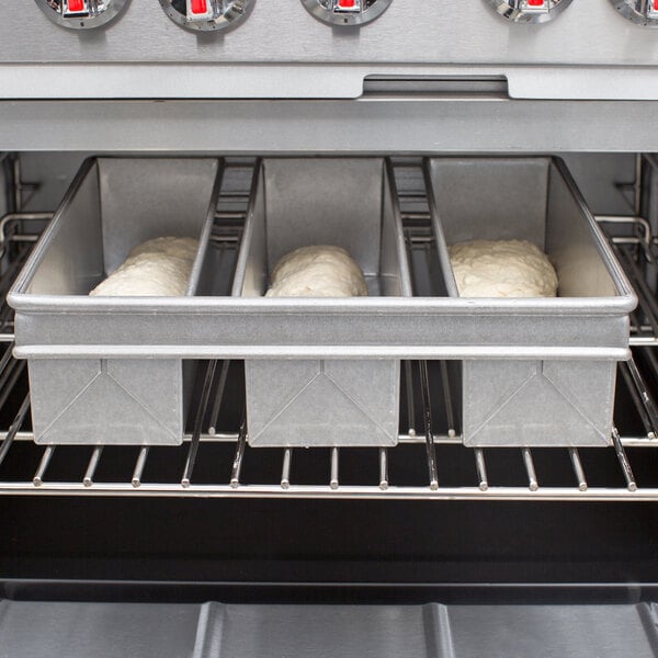 A Chicago Metallic aluminized steel bread loaf pan with three loaves of bread in it sitting in an oven.