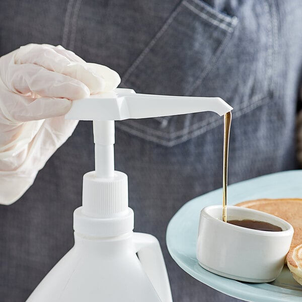 A person using a Carlisle .5 oz. condiment pump to pour syrup onto a small dish of pancakes.