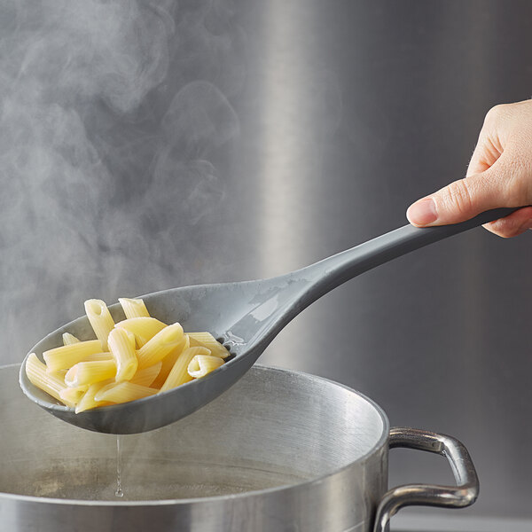A hand holding a Tablecraft flexible silicone spoon of pasta over a pot of water.