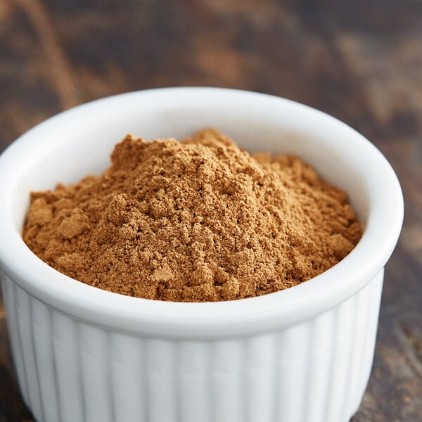 A white bowl of Regal Five Spice powder on a wooden table.