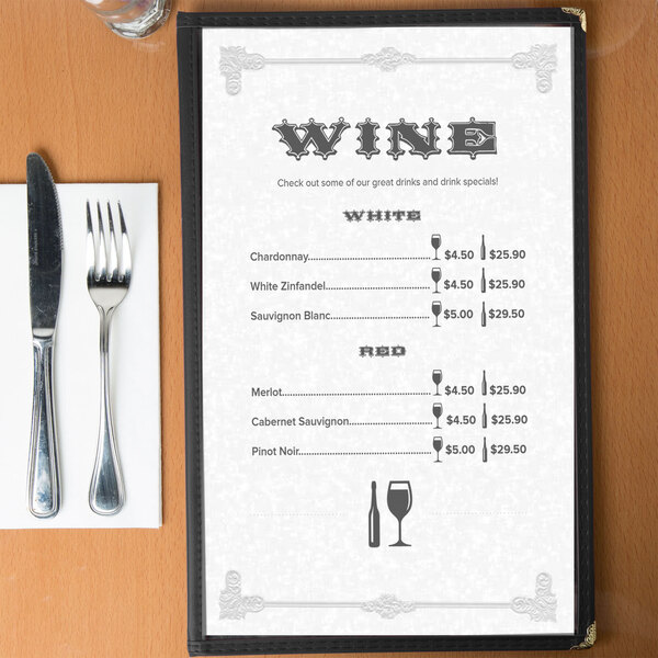 A black menu with a scroll border on a table with silverware and a napkin.