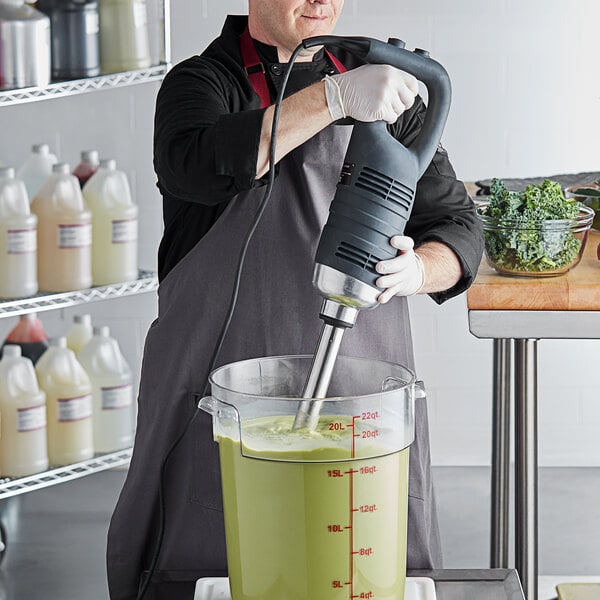 A man using an AvaMix heavy-duty immersion blender to mix green liquid in a bowl.