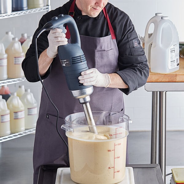 A man using an AvaMix heavy-duty immersion blender to mix liquid in a bowl.