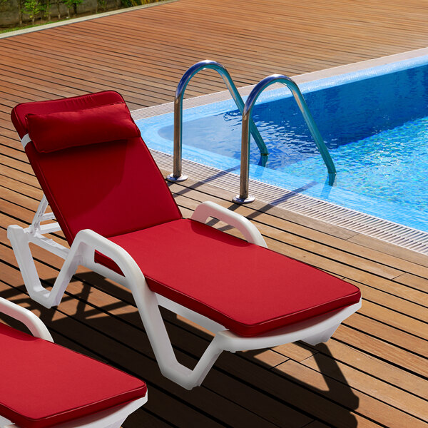 Two white Lancaster Table & Seating chaise loungers with red cushions next to a pool.