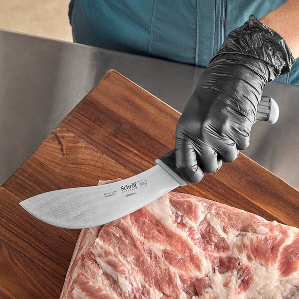 A person in black gloves using a Schraf skinning knife to cut a piece of meat on a wooden surface.