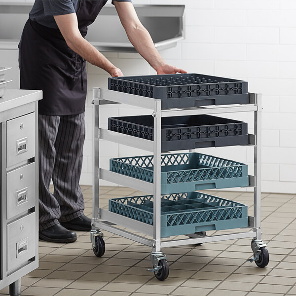 A man pushing a Steelton glass rack cart with a tray on a counter in a professional kitchen.