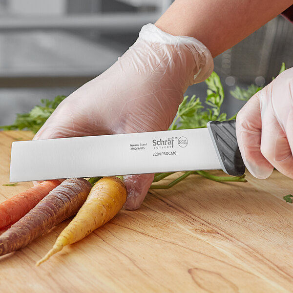 A person in plastic gloves uses a Schraf produce knife to cut carrots on a wooden surface.