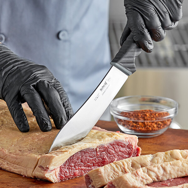 A person in black gloves using a Schraf butcher knife to cut meat on a cutting board.