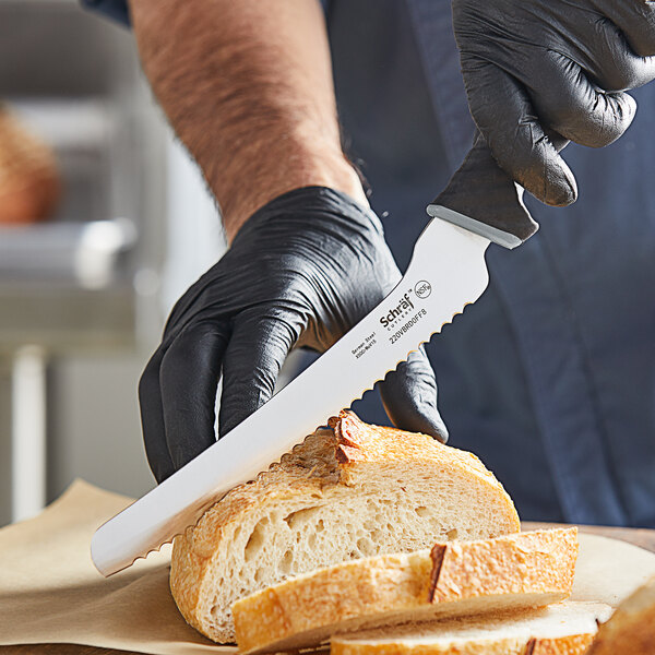 A person in black gloves uses a Schraf serrated bread knife to cut a piece of bread.