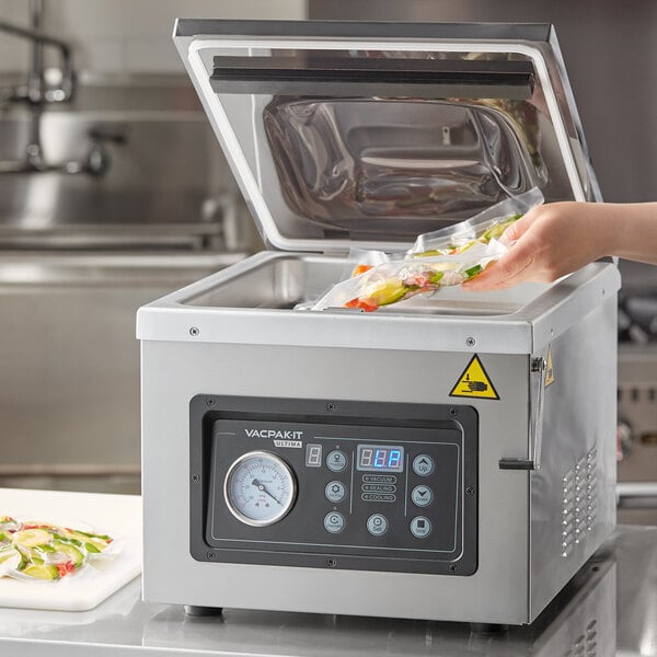 A hand using the VacPak-It Ultima vacuum packaging machine to seal food in a bag.