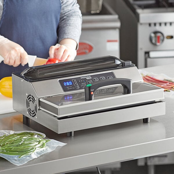 A woman using a VacPak-It vacuum packing machine to cut vegetables on a counter in a professional kitchen.