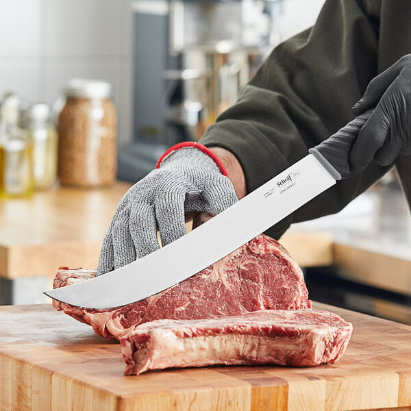 A person using a Schraf Cimeter knife to cut meat on a wooden surface.