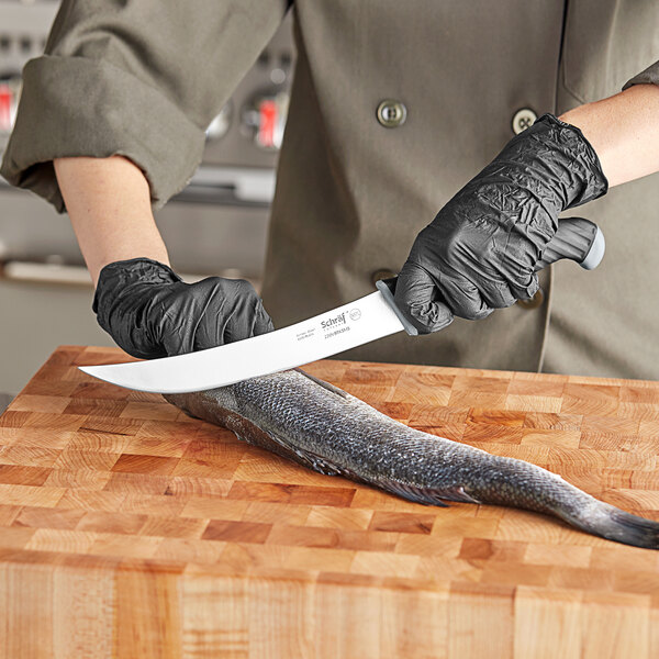 A person in black gloves using a Schraf Breaking Knife to cut a fish on a cutting board.