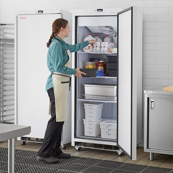 A woman wearing an apron opening a Galaxy white reach-in refrigerator.