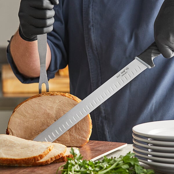 A person in gloves using a Schraf slicing knife to cut meat on a counter.
