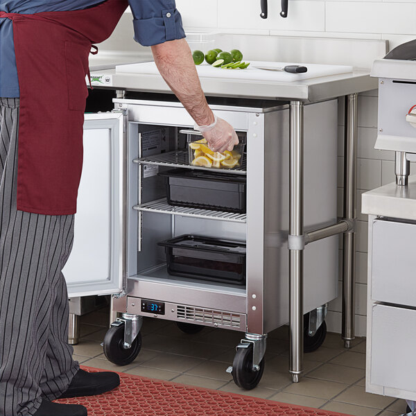 A man in a chef's outfit puts lemons in a Beverage-Air undercounter refrigerator in a professional kitchen.