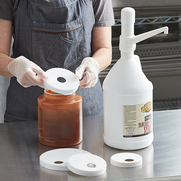 A person in gloves using a Tablecraft condiment pump to fill a jar with brown liquid.