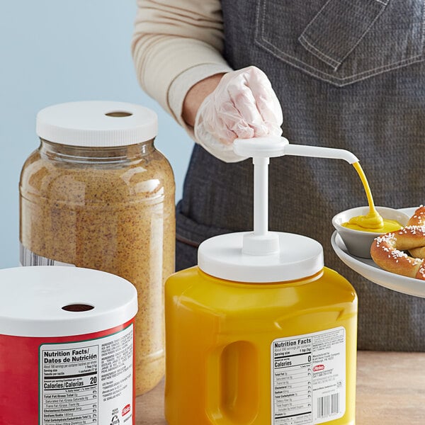 A person using a Tablecraft condiment pump to pour mustard into a white container.