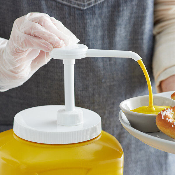 A person using a Tablecraft condiment pump to pour yellow liquid onto a plate of food.