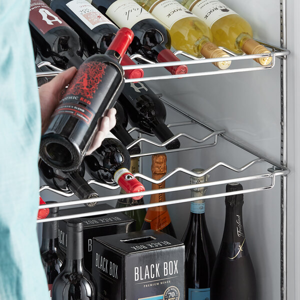 A person holding a bottle of wine in a Beverage-Air black curved wine rack.