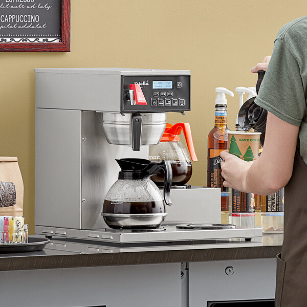 A woman pouring coffee into an Estella Caffe commercial coffee maker with 3 decanter warmers.