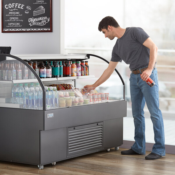 A man standing in front of an Avantco Black Horizontal Air Curtain Merchandiser filled with drinks.