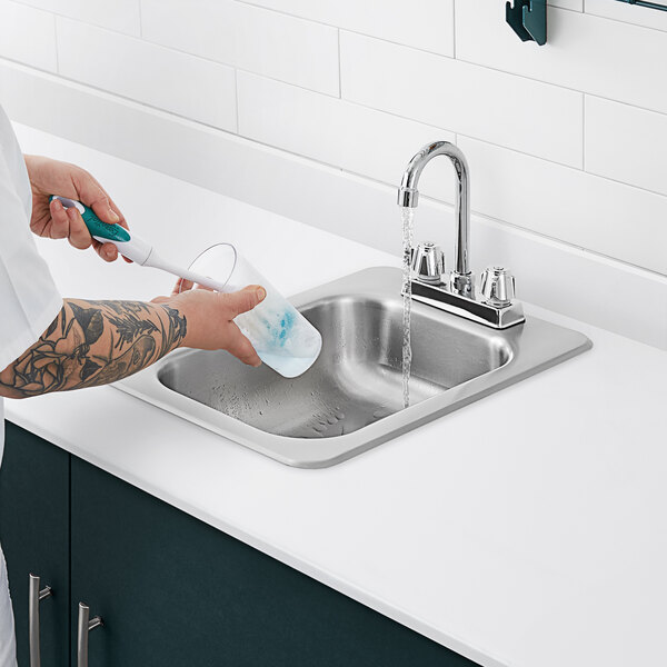 A man with tattoos washing his hands in a Regency stainless steel drop-in sink with a gooseneck faucet.