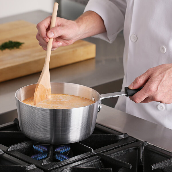 A person stirring food in a Choice aluminum sauce pan on a stove.